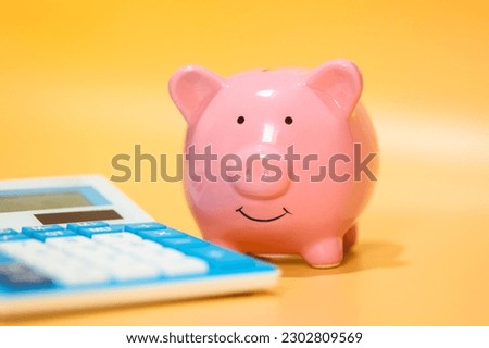 A ceramic piggy bank and a blue calculator. Studio photo. Orange background. Close-up photo.
