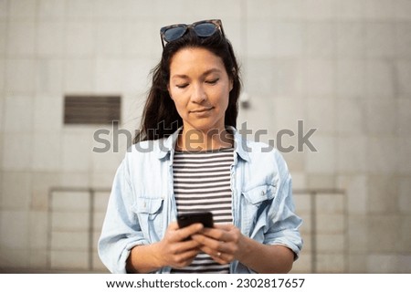 Close-up portrait of beautiful young asian woman reading text message on mobile phone outside in the city