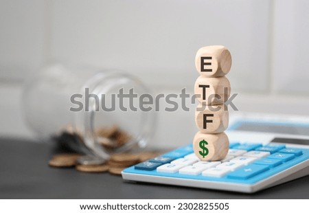 The acronym ETF and the money symbol written on wooden dice lying on top of a calculator.
