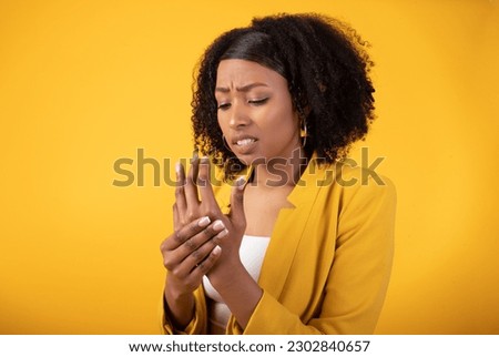 Numbness of the limbs. Black lady suffering from pain in the hand, palm and joints, woman holding a wrist in her hand, standing on yellow background. Wrist injuries, carpal tunnel syndrome, neuralgia