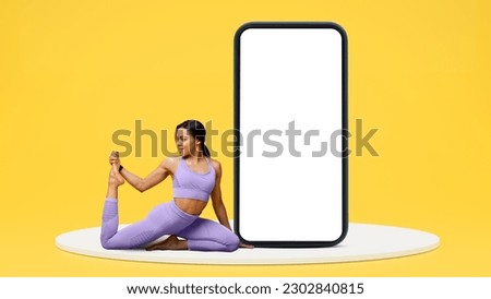 Happy young african american slim woman in sportswear doing leg stretch on platform near smartphone with blank screen isolated on yellow studio background. Body care app for weight loss and fitness Royalty-Free Stock Photo #2302840815