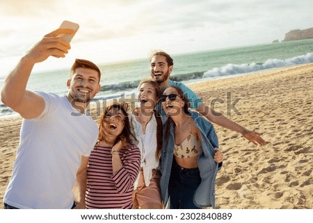 Happy millennial european and arabic friends have fun, taking selfie on smartphone, enjoy free time on ocean beach. App for blog and social network, outdoor party, holiday and trip Royalty-Free Stock Photo #2302840889