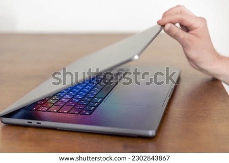 A man's hand opens a laptop with a multi-colored glowing screen.