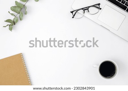Flat lay white background with laptop, notepad, coffee cup and glasses.