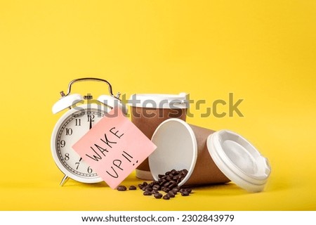 Alarm clock, paper cup, paper reminder and coffee beans on yellow background.