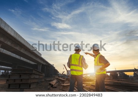 Asian architect and mature supervisors meeting at construction site Multiethnic workers and engineers discussing plans Two construction workers working together while visiting expressway construction Royalty-Free Stock Photo #2302849483