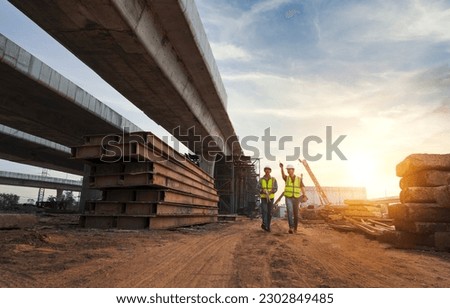 Asian architect and mature supervisors meeting at construction site Multiethnic workers and engineers discussing plans Two construction workers working together while visiting expressway construction Royalty-Free Stock Photo #2302849485