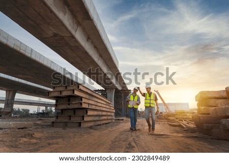 Asian architect and mature supervisors meeting at construction site Multiethnic workers and engineers discussing plans Two construction workers working together while visiting expressway construction Royalty-Free Stock Photo #2302849489