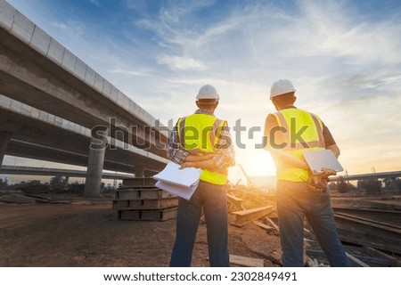 Asian architect and mature supervisors meeting at construction site Multiethnic workers and engineers discussing plans Two construction workers working together while visiting expressway construction Royalty-Free Stock Photo #2302849491