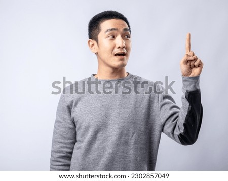 A portrait of an Asian man wearing a gray sweater pointing in a specific direction with one hand. Isolated with a white background.