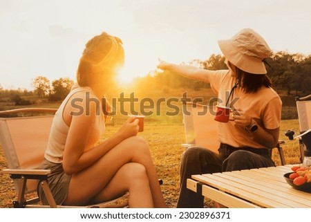 Wonderful evening moment : Two asian female friends sitting and chatting cheerfully drinking freshly brewed coffee watching the beauty of nature mountain forest and sunset on vacation trip. Royalty-Free Stock Photo #2302896371