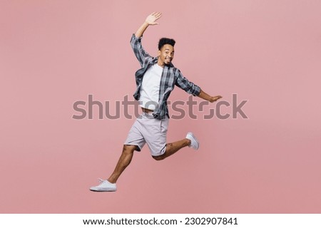 Full body young man of African American ethnicity he wear blue shirt look camera jump high like flying with outstretched hands isolated on plain pastel light pink background. People lifestyle concept Royalty-Free Stock Photo #2302907841