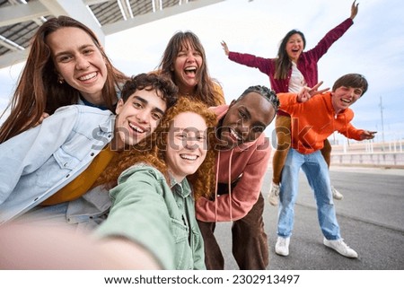 Group of happy multiracial friends taking a selfie photo with cell phone outside. Happy young people together smiling at camera. Youth concept with boys and girls having fun walking along city street. Royalty-Free Stock Photo #2302913497