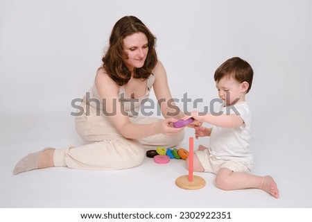 Happy baby with mother play educational toys on studio white background. Portrait of a smiling child with mom and playing while sitting on the floor. Kid about two years old (one year nine months)