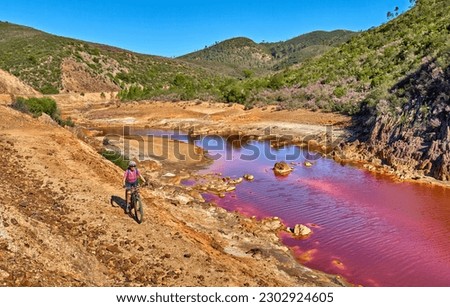 nice woman with electric mountain bike on a bike tour along river Rio Tinto with its natural red water in Andalusia, Spain