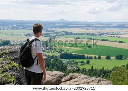 A young man standing on the top of the mountain in the natural park Bohemian Paradise looking down to the valley. Czech Republic, Europe. Summer holidays  Český Ráj, Česká republika.