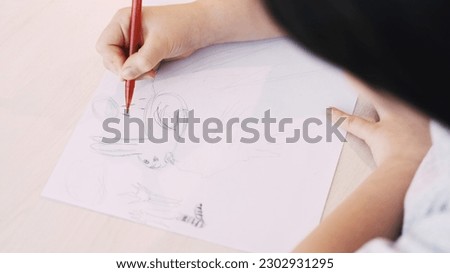 Cute picture. Kids painting. Art hobby. Unrecognizable child drawing rabbit on white paper with pencil sitting table.