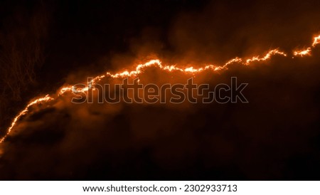 Night fire in the forest with fire and smoke.Epic aerial photo of a smoking wild flame.A blazing,glowing fire at night.Forest fires.Dry grass is burning. climate change,ecology.Line fire in the dark. Royalty-Free Stock Photo #2302933713
