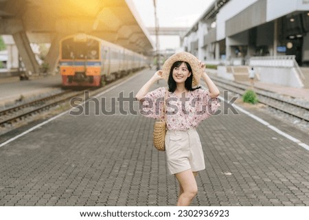 asian young woman traveler with weaving basket happy smiling and looking to a camera beside train coming background. Journey trip lifestyle, world travel explorer or Asia summer tourism concept.