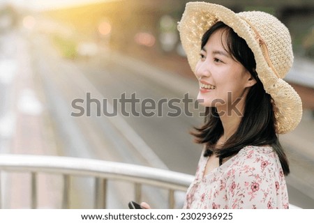 asian young woman traveler with weaving basket using mobile phone and standing on overpass with railway background. Journey trip lifestyle, world travel explorer or Asia summer tourism concept.