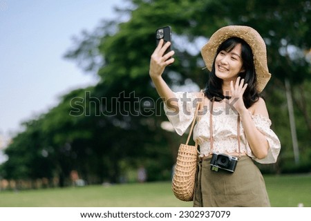 Portrait of young asian woman traveler with weaving hat, basket, mobile phone and camera on green public park background. Journey trip lifestyle, world travel explorer or Asia summer tourism concept.