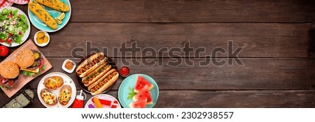 Summer BBQ food corner border. Hamburgers, hot dogs, potatoes, corn and cold treats. Top down view over a dark wood banner background. Copy space.