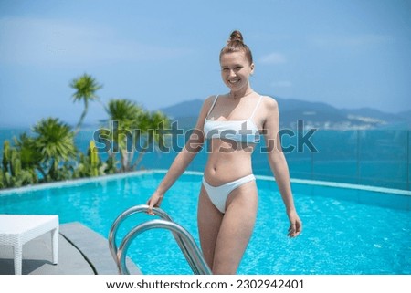 beautiful young woman relax in a swimsuit on the roof, near pool, sunbathing in summer day, sea and islands background, luxury hotel