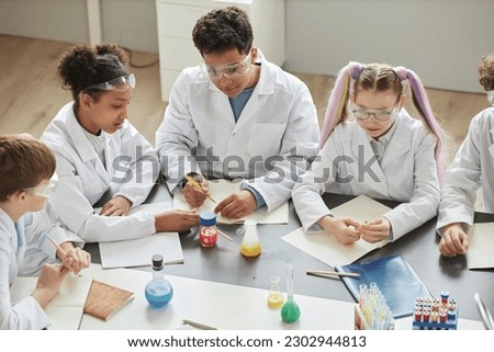 Top view at diverse group of children doing experiments during science class in school and wearing lab coats