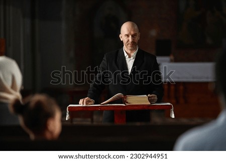 Mature pastor reading Bible for believers while standing at altar in church Royalty-Free Stock Photo #2302944951