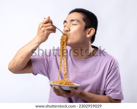 A portrait of a happy Asian man wearing a purple shirt while eating noodles. Isolated with a white background. Royalty-Free Stock Photo #2302959029