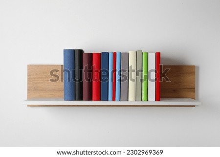 Many hardcover books on wooden shelf near white wall Royalty-Free Stock Photo #2302969369