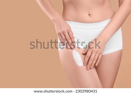 Woman with smear of body cream on her leg against light brown background, closeup. Space for text