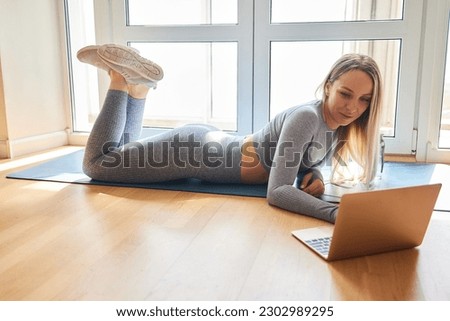 Enduring concentrated sporty woman is doing working out at home and doing plank in front of her laptop, wearing sport outfit