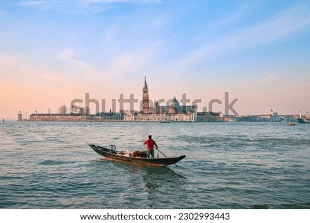 The photo depicts a gondola driver navigating the sea at dawn, with the iconic city of Venice in the background, creating a stunning view that conveys tranquility and romance.