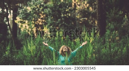 One happy woman alone in the green forest celebrating nature and freedom alone raising her arms. Healthy and wellbeing lifestyle people in outdoors leisure activity. Concept of environment and life Royalty-Free Stock Photo #2303005545