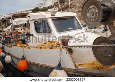 A white fishing boat with fishing nets and floats on the sides of the boat in the harbor