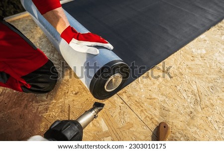 Roof Worker with Roll of EPDM Rubber Membrane Material Preparing to Cover Plywood Roof Royalty-Free Stock Photo #2303010175