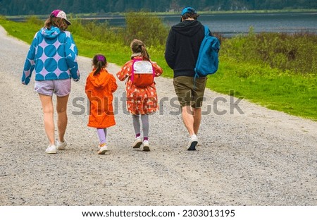 Mother, father and daughters walking in the Park and enjoying the beautiful nature. Rear view of a happy young family with two children walking on a road. Camping, hiking, travel photo, copyspace