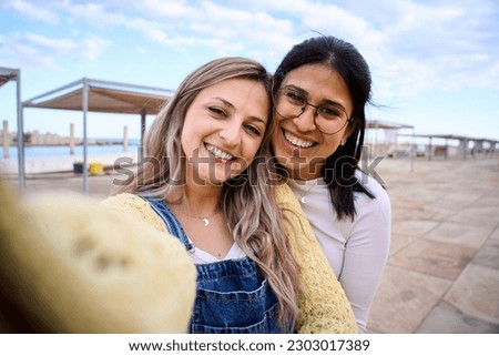 Happy LGBT lesbian Caucasian couple on tourist vacation taking selfie with mobile phone on promenade. People in love and romantic attitude. Generation z and social media photo apps.