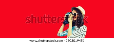 Summer portrait of happy smiling young woman photographer with film camera wearing summer straw hat on red background, blank copy space for advertising text
