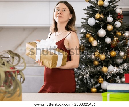 Positive young woman with a present in her hands poses at home against the background of a Christmas tree