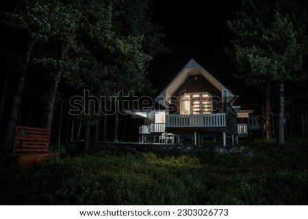 Mountain night landscape of building at forest at night with moon or vintage country house at night with clouds and stars. Cold Autumn night