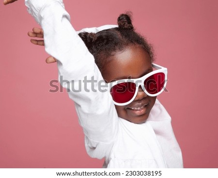  A delightful studio shot of a 6-year-old African-American girl of Ethiopian descent. Against a vibrant pink paper background, she captures attention with her charming smile, and huge sunglasses.