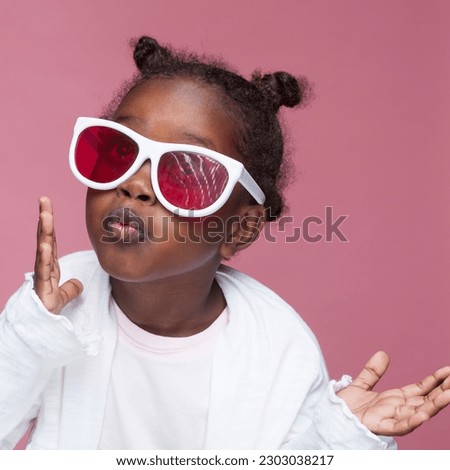  A delightful studio shot of a 6-year-old African-American girl of Ethiopian descent. Against a vibrant pink paper background, she captures attention with her charming smile, and huge sunglasses.