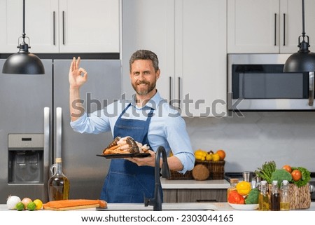 Man in cook apron cooking seafood crab and shrimp, salmon and lobster in kitchen. Happy chef in cook apron cooking seafood. Cook in chef apron on kitchen with salmon fillet. Salmon recipes.
