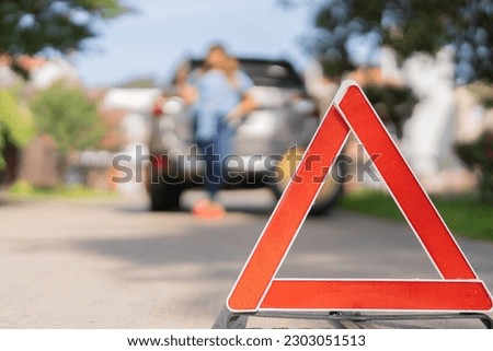 Woman wearing a safety triangle waiting for the tow truck to pick up her car, because it stopped working.