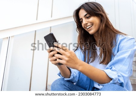 Happy young caucasian woman looking mobile phone sitting on stairs in street. Copy space.