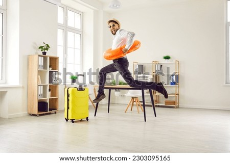 Happy, funny, energetic, excited man office worker in a sun hat, sunglasses and beach ring jumping and having fun in the office. Summer holiday, vacation, work leave, annual leave concept Royalty-Free Stock Photo #2303095165