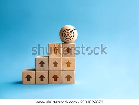 Rise up arrows shoot up towards the goal. Target icon on wooden sphere, top of wood cube block bar graph chart steps on blue background. Business growth process, trend, economic improvement concepts.