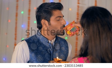 A modern newly-wed couple happily celebrating the Karwa Chauth festival together. Over the shoulder shot - Indian wife in saree and husband in kurta pajama. Decorated background